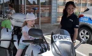 dziewczynka na policyjnym motocyklu, obok policjantka. Pozują do zdjęcia