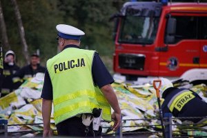 policjant w kamizelce zabezpiecza ulicę, w tle akcja gaśnicza