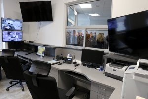 Zdjęcie przedstawia dyżurkę w nowym komisariacie.  Na biurku stoją monitory, drukarki, telefony.