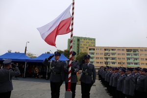 Policjanci stoją przy maszcie z flagą Polski.