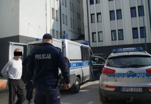 fot. 41-letni mężczyzna podejrzany o pozbawienie wolności kobiety oraz policjanci, w tle radiowozy