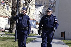 Dwóch policjantów patrolują ulicę, jeden z nich rozmawia przez radiostację.