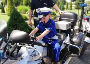 chłopiec siedzi na policyjnym motorze, obok stoi policjant