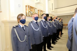 Wyróżnieni policjanci w mundurach galowych z założonymi maskami na usta i nos.