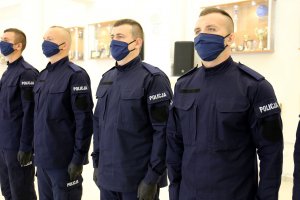 Nowi policjanci ubrani w granatowe mundury z założonymi maseczkami zakrywającymi usta i nos.