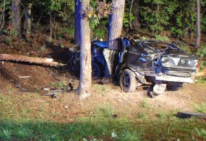 Uszkodzony samochód stoi pomiędzy drzewami. Jedno z nich wbite jest w karoserie