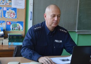 policjant siedzi przed laptopem w szkolnej klasie