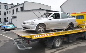 samochód marki Opel Vectra na lawecie, w tle policyjny radiowóz i ściana budynku.