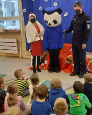 policjant, maskotka i nauczycielka stoją przed dziećmi