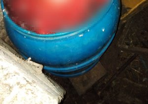 stojąca w kącie pomieszczenia niebieska plastikowa beczka z zawartością czerwonej cieczy z pływającymi wewnątrz kawałkami mięsa