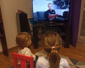 dwoje małych dzieci siedzi przed telewizorem, na którym widać policjanta czytającego książkę
