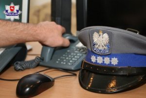 policjant odbiera telefon na dyżurce, w tle czapka służbowa