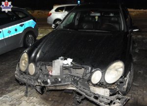 samochód osobowy z uszkodzonym w wyniku kolizji przodem, obok stoi policyjny radiowóz