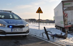 radiowóz, uszkodzony rower leżący na drodze i samochód ciężarowy stojący poza drogą