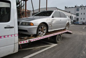 samochód marki BMW na lawecie, w tle budynek i radiowozy