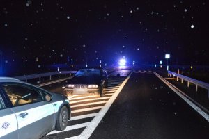 Pora nocna oznakowany radiowóz policji oraz uszkodzony samochód osobowy marki BMW stoją na jezdni.