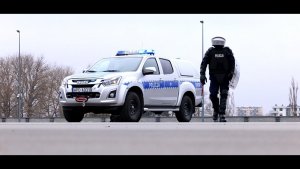 Policjant z Oddziału prewencji Policji w Lublinie idzie obok radiowozu oznakowanego. Funkcjonariusz ma w ręku tarcze na głowie kask ochronny.