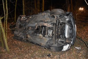 samochód  leży na boku  w lesie, widoczne uszkodzenia, między innymi tylnego prawego koła , uszkodzenia podwozia.