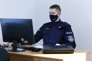 Policjant w maseczce przy biurku patrzy w ekran monitora.