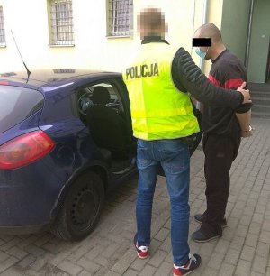 policjant i zatrzymany mężczyzna w kajdankach przy samochodzie