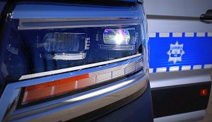 Lewa przednia lampa nowego radiowozu marki Volkswagen Crafter w tle drzwi pojazdu z napisem policja.