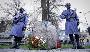Dwóch policjantów z bronią długą stoi obok pomnika.
