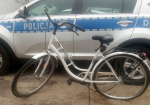 Odzyskany przez policjantów rower zabezpieczony na policyjnym parkingu. W tle oznakowany policyjny radiowóz.