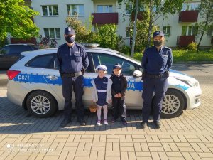 Policjanci i dwoje dzieci stojący przy radiowozie, w tle blok mieszkalny
