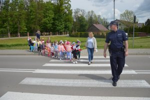 policjant uczy przedszkolaki przechodzenia przez przejście. W tle przedszkolanka.