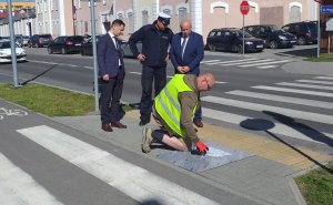 policjant i trzej mężczyźni przy przejściu dla pieszych. Jeden z mężczyzn maluje farbą chodnik przed przejściem dla pieszych