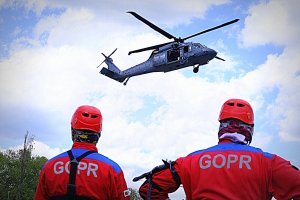 Dwóch ratowników GOPR w czerwonych kombinezonach patrzą na lecącego Black Hawk.