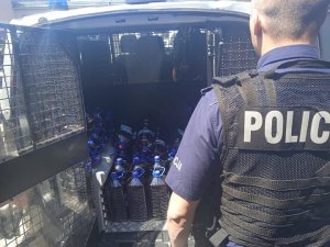 policjant stoi przy radiowozie, wewnątrz którego widoczne są butelki z zabezpieczonym alkoholem