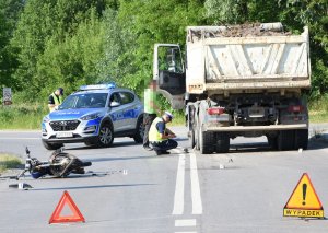 rozbity motorower na szosie obok ciężarówka radiowóz i dwóch policjantów piszących protokoły