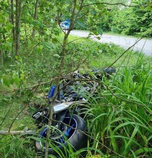 zniszczony motocykl leżący w zaroślach na poboczu jezdni