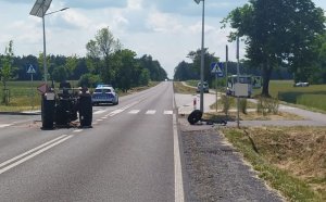 Uszkodzony ciągnik rolniczy na pasie jezdni. Na dalszym tle oznakowane radiowozy policji