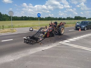 Uszkodzony ciągnik rolniczy z wyrwanym przednim zawieszeniem na pasie jezdni