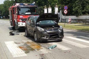 Uszkodzony Ford Kuga stoi na jezdni przed przejściem dla pieszych, za nim wóz Straży Pożarnej