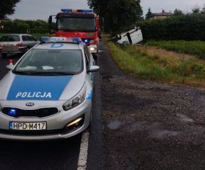 radiowóz i pojazd straży pożarnej stojące na drodze, w dalszej perspektywie w rowie dachujące auto koloru białego