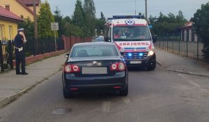 Na pierwszym planie pojazd marki Volkswagen Jetta ustawiony tyłem. Po prawej policjant ruchu drogowego. W tle karetka pogotowia ratunkowego..