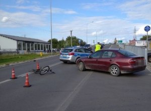 miejsce wypadku, samochód osobowy i przewrócony rower na jezdni, w oddali radiowóz i policjanci