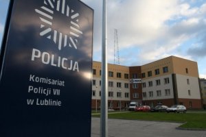 Zdjęcie przedstawia tablicę z napisem siódmy komisariat policji w Lublinie. W drugim planie zdjęcia budynek siódmego komisariatu policji w Lublinie.