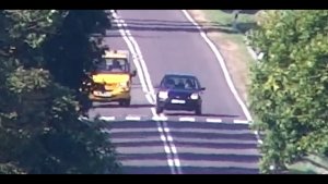 Stop klatka z filmu nagranego przez drona. Osobowe auto wyprzedza inny pojazd na przejściu dla pieszy.