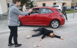 samochód na chodniku za przejściem dla pieszych na jezdni leży młoda kobieta - inscenizacja wypadku drogowego