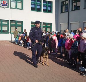 policjant z psem służbowym idący wzdłuż ustawionych w grupie  dzieci