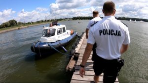 Dwóch policjantów idzie pomostem do łodzi policyjnej na Zalewem Zemborzyckim