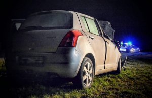 uszkodzony samochód marki Suzuki Swift w tle radiowóz z włączonymi sygnałami świetlnymi