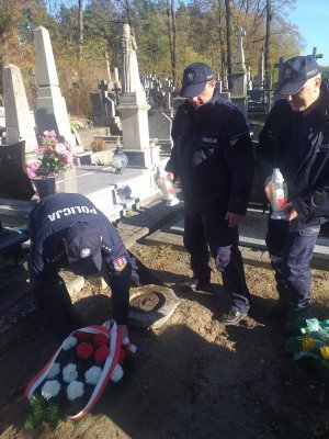 policjanci kładą wiązankę i znicz na grobie zmarłego policjanta