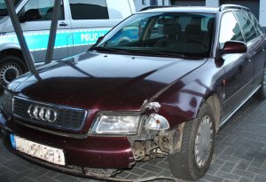 samochód marki Audi z uszkodzonymi elementami karoserii, w tle radiowóz