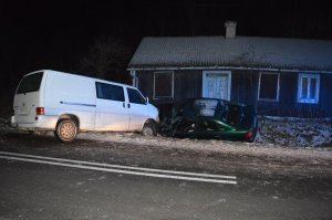 Stojące w rowie na tle drewnianego domu dwa samochody, które zderzyły się przodem.