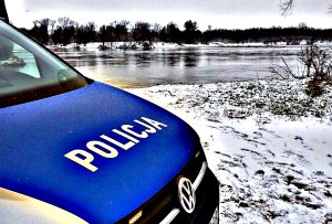 Radiowóz oznakowany z napisem na masce policja w tle zamarzająca rzeka.